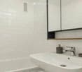 Modern bathroom with a white sink, chrome faucet, soap dispenser, and a large mirror with wooden frame.