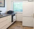 Modern kitchen with white cabinets, stainless steel sink, oven, refrigerator, and tiled floor.