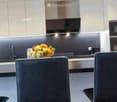 Modern kitchen with stainless steel appliances, a fruit bowl on the counter, and four black chairs around a dining table.
