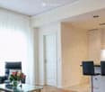 Modern living and dining area with a sofa, glass coffee table, and a kitchen counter with bar stools.