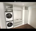 A small, well-organized room with a built-in wardrobe and a private washing machine. The wardrobe has multiple shelves and a hanging space, while the washing machine is neatly stacked with a dryer above it.