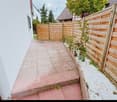 Narrow pathway bordered by wooden fences, small plants, and gravel beds.