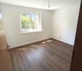 Empty room with wooden flooring, white walls, and a window with white frame. Natural light streams in, illuminating the space.