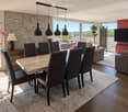 Modern living and dining area with a stone accent wall, large windows, a dining table with six chairs, a sofa, a television, and decorative vases.
