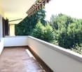 Balcony with tiled floor, white walls, metal railing, and a view of lush greenery.