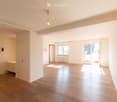 Empty room with light wooden flooring, white walls, and large windows allowing natural light. Features include a sliding glass door leading outside, a built-in cabinet, and recessed ceiling lighting.
