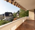 Balcony with tiled flooring, wooden shutters, and a view of neighboring houses and greenery.