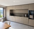 Modern kitchen with light grey cabinets, a wooden dining table, white chairs, and various appliances including a coffee maker, refrigerator, and oven.