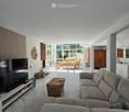 Bright living room with large windows, grey sectional sofa, coffee table, TV, and dining area visible through an open space.