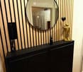 A stylish hallway or entryway with a large round mirror, a black cabinet, a golden statue, and a decorative vase.