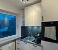 Modern kitchen with white cabinets, stainless steel sink, oven, and coffee maker on the counter. A large window provides natural light.