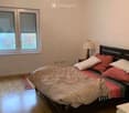 Cozy bedroom with a double bed, pillows, a nightstand, and a lamp. The room features wooden flooring and a window with blinds.