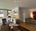 Open-plan living and dining area with a sofa, dining table, chairs, and a modern kitchen featuring white cabinets, a microwave, oven, and sink.