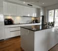 Modern kitchen with white cabinets, black countertop, stainless steel sink, and various appliances including a microwave and coffee maker. A potted plant is placed on the windowsill.