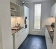 Modern kitchen with white cabinets, dark tiled floor, and stainless steel appliances. Features an oven, sink, and teapot on the counter.