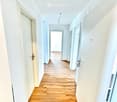 Empty hallway with light wooden flooring, white walls, and multiple doors on both sides.