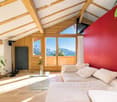 Bright living room with wooden beams, large windows offering mountain views, white sofa, glass coffee table, floor lamp, and potted plant.