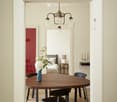 Dining room with a round wooden table, black chairs, a chandelier, and a fireplace visible in the background.