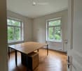Bright room with wooden flooring, large windows, a long wooden table, and a small cabinet.