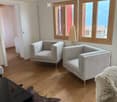 Modern living room with wooden floors, large windows, grey sofa, armchairs, coffee table, and a floor lamp.