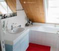 Bathroom with a white sink, bathtub, and wooden slanted ceiling. Includes a red bath mat, toothbrush holder, and small basket on the counter.