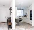 Modern, open-plan living and dining area with white walls, tiled flooring, and contemporary furniture including a dining table, chairs, and built-in cabinets.