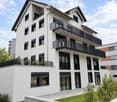 Modern two-story residential building with white facade, black railings, multiple balconies, and contemporary design.