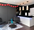 Modern reception area with dark grey walls, white reception desk, black leather sofa and chair, glass coffee table with decorative vases, and pendant lights.