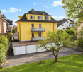Two-story yellow house with white-framed windows, a balcony, and a garage attached to the side.
