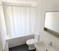 Modern bathroom with white tiles, dark grey floor, toilet, sink, bathtub, shower curtain, and radiator.