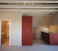 Modern kitchen with red cabinets, a sink, and an oven. An open doorway leads to a small bathroom with a toilet and sink.