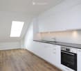 Modern kitchen with white cabinets, wooden flooring, and a skylight window above the sink.