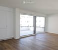 Empty room with wooden flooring, white walls, large sliding glass doors leading to a balcony, and built-in white cabinetry.