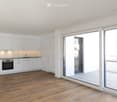 Modern kitchen with white cabinets, wooden flooring, and a large glass sliding door leading to a tiled area.