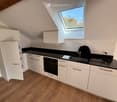 Modern kitchen with white cabinets, black countertops, wooden flooring, and a skylight window above the sink.