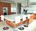 Modern kitchen with a white island, four white stools, stainless steel appliances, wooden cabinets, and a sleek design.