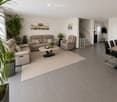 Modern living room with grey tiled floor, beige sofa, armchair, coffee table, dining area with chairs and table, and decorative plants.