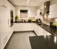 Modern kitchen with white cabinets, black countertops, stainless steel appliances, and a window with blinds. Includes an oven, sink, coffee maker, induction stove, and potted plants.