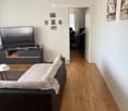 Living room with a grey sofa, a small table, a TV, and a chair in the background. The room has wooden flooring and white walls.