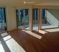 Empty room with wooden flooring, large glass sliding doors leading to a balcony, and natural light streaming in.