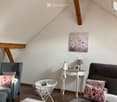 Cozy attic living room with slanted wooden ceiling, grey sofa, armchair, small white table, lamp, and decorative items.