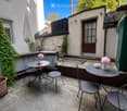 A small, enclosed patio with tiled flooring, two round tables with chairs, vases with pink flowers, and an umbrella leaning against the wall.
