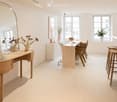 Modern, minimalist room with a vanity table, a large mirror, a marble dining table with chairs, and wooden stools near a window.