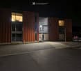 modern building, brown exterior, large windows, illuminated at night, gravel parking lot, street light