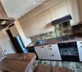 Modern kitchen with light-colored cabinets, wooden countertops, a sink, stove, oven, and a small wooden table.