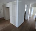 Empty hallway with wooden flooring, white walls, and built-in white cabinetry on one side. Open doorways lead to adjacent rooms.