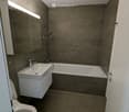 Modern bathroom with a toilet, sink, bathtub, and mirror. Features grey tiled walls and a sleek, contemporary design.