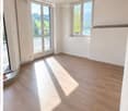 Empty room with wooden flooring, large windows, and a sliding glass door leading to a balcony. The walls are white, and the room is well-lit with natural light.