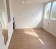 Empty room with light wooden flooring, white walls, and large windows allowing natural light. No furniture or equipment present.