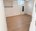 Empty room with wooden flooring, white walls, and a single white door. No furniture or equipment present.